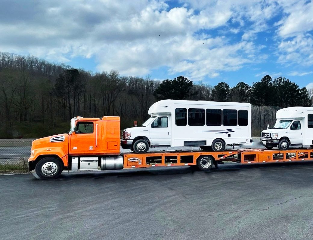 orange semi truck carrying 2 white buses