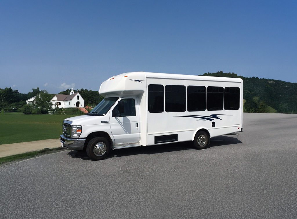 White church shuttle bus parked on a road near a chapel.