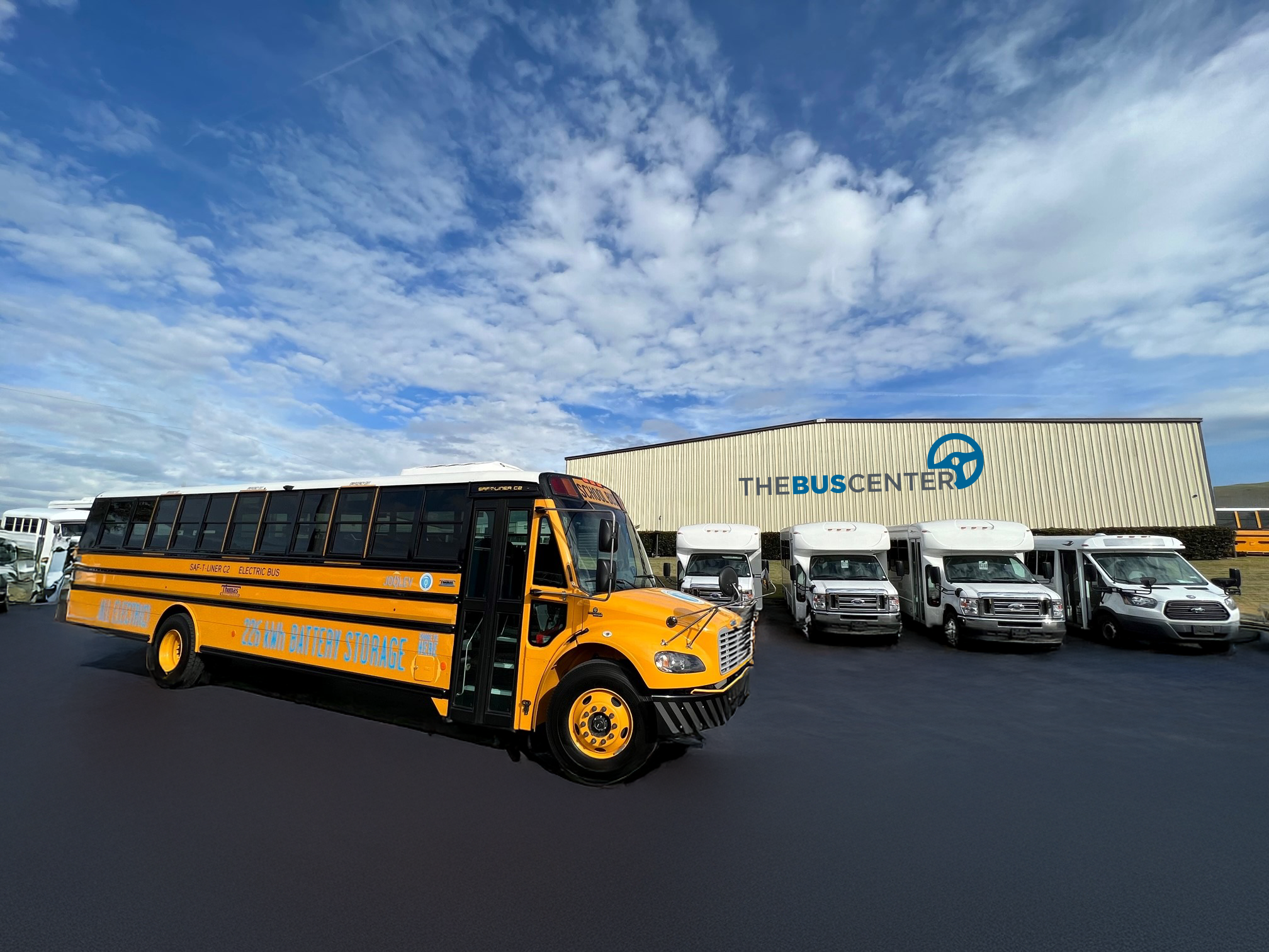 Electric school bus and commercial vans parked outside The Bus Center building.