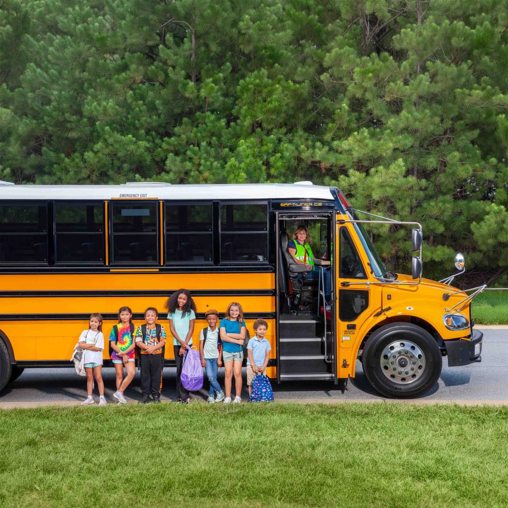 Students standing next to a yellow school bus with driver in doorway.